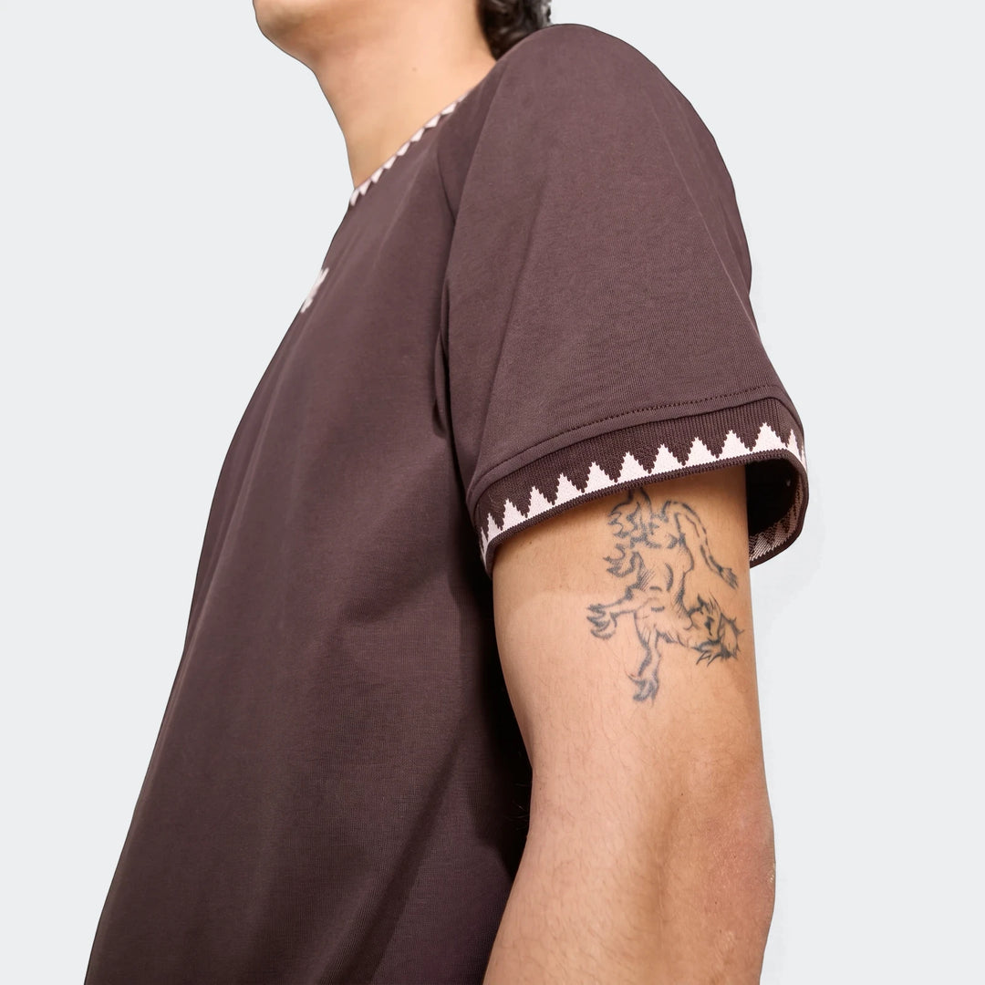 Close-up of a person wearing a brown Chest Stripe Short Sleeve T-Shirt with white triangular patterns on the collar and