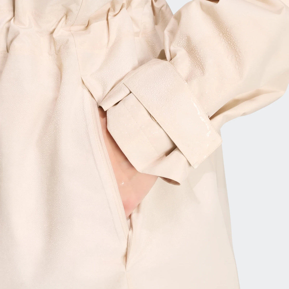 Close-up of a beige City Rain Parka showcasing its water-resistant textured fabric, zippered pocket with a hand, and folded