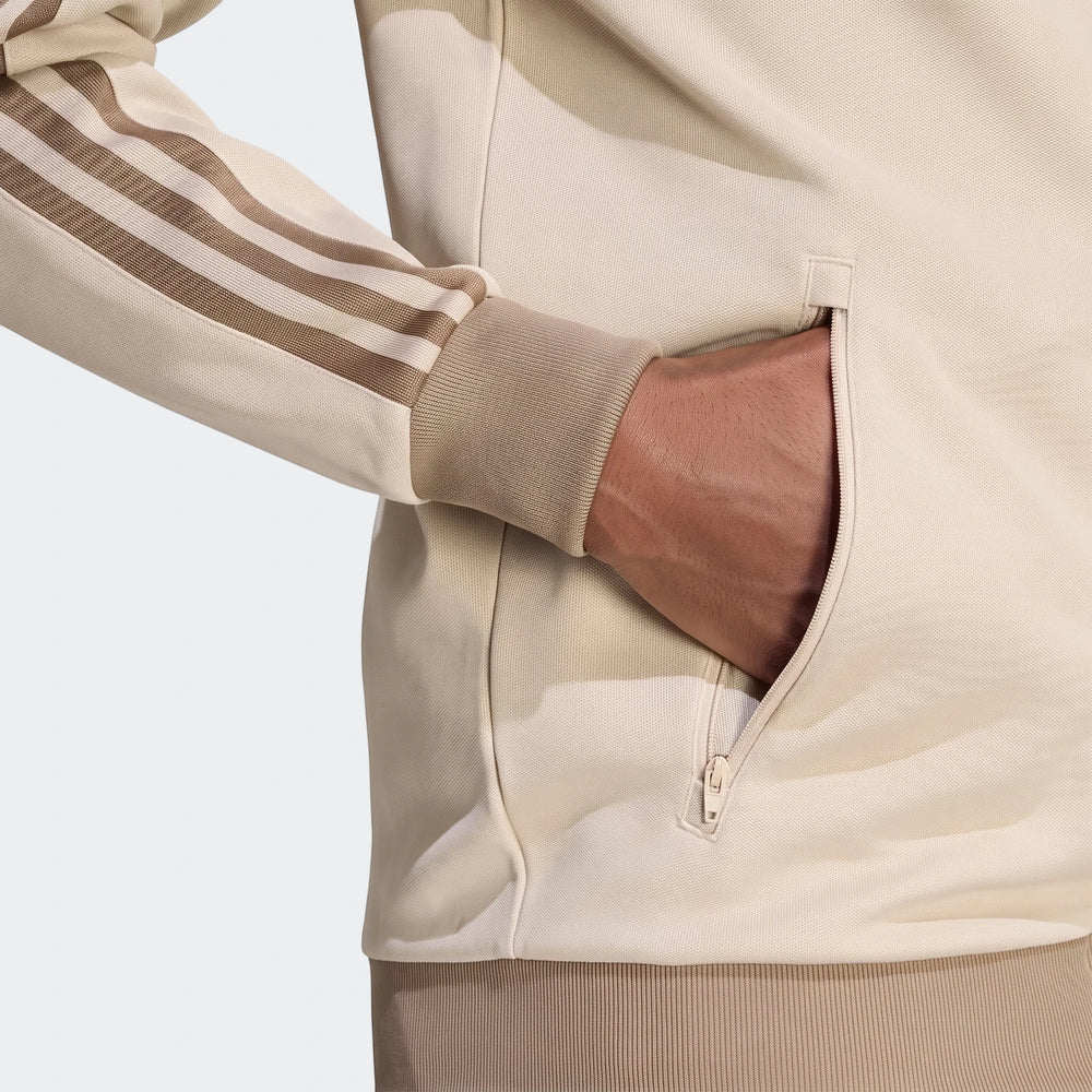 Close-up of a beige Classic Track Top with brown stripes on the sleeve and a hand in the zippered side pocket.