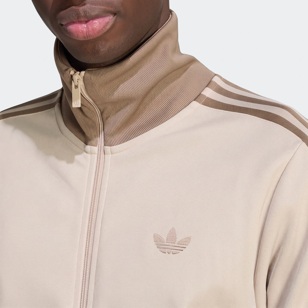 Close-up of a beige Classic Track Top worn by a person, featuring a stand-up collar, front zipper, and three shoulder