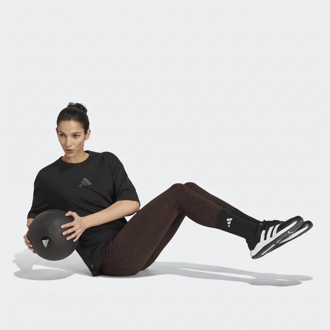 Woman in a black adidas Climacool Animal Training Graphic T-Shirt and patterned leggings exercising with a medicine ball.