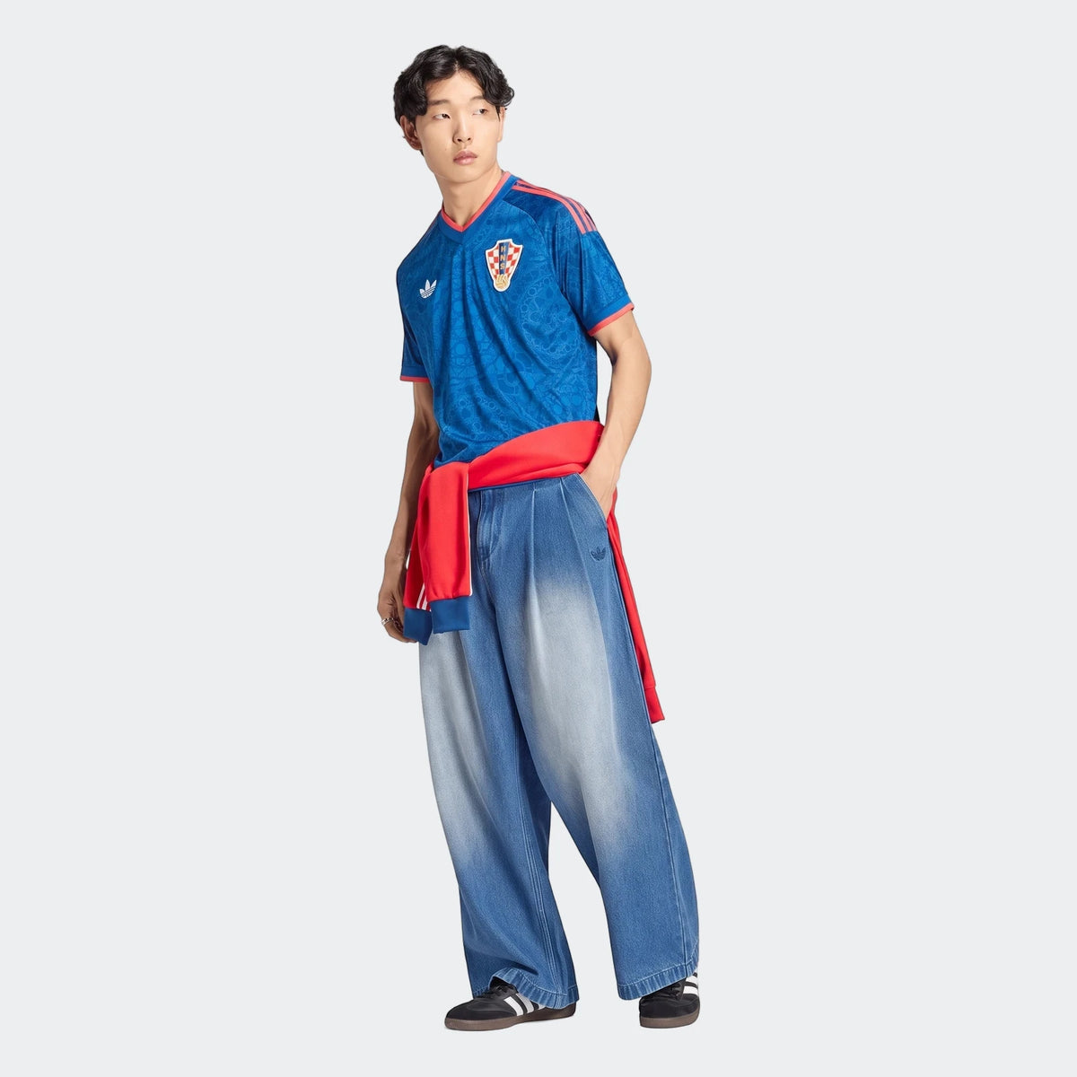 Young Asian man modeling a blue Adidas Croatia 26 Away Jersey with red details, baggy faded jeans, and a red sweatshirt.