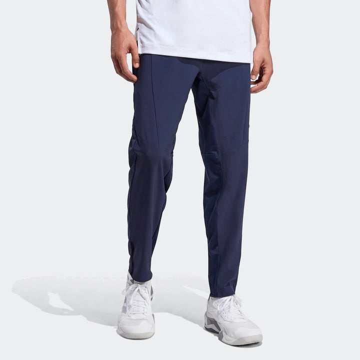 Man models dark blue D4T Hybrid Pants paired with white sneakers in a studio setting, showcasing the fit and design.