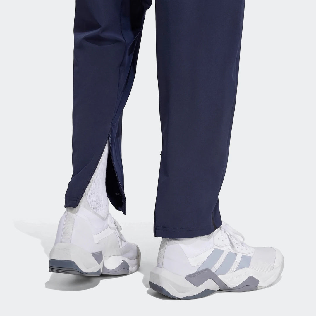 Close-up of a person wearing navy D4T Hybrid Pants with partially unzipped ankles and white athletic sneakers.