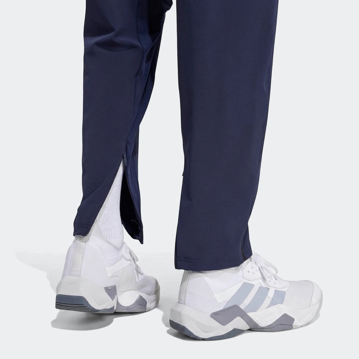Close-up of a person wearing navy D4T Hybrid Pants with partially unzipped ankles and white athletic sneakers.