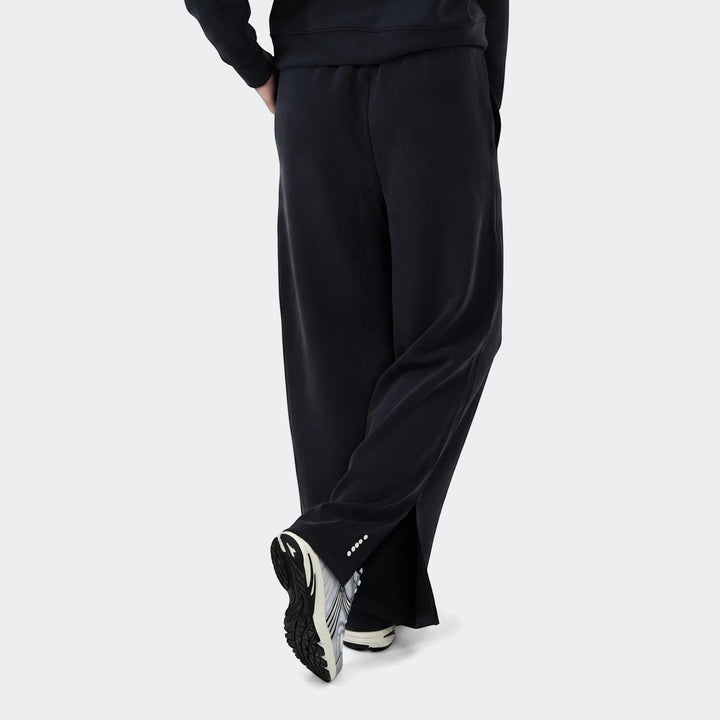 Danielle Trackpant in black with relaxed fit, elastic waistband and tapered leg, shown from the side with sneakers.