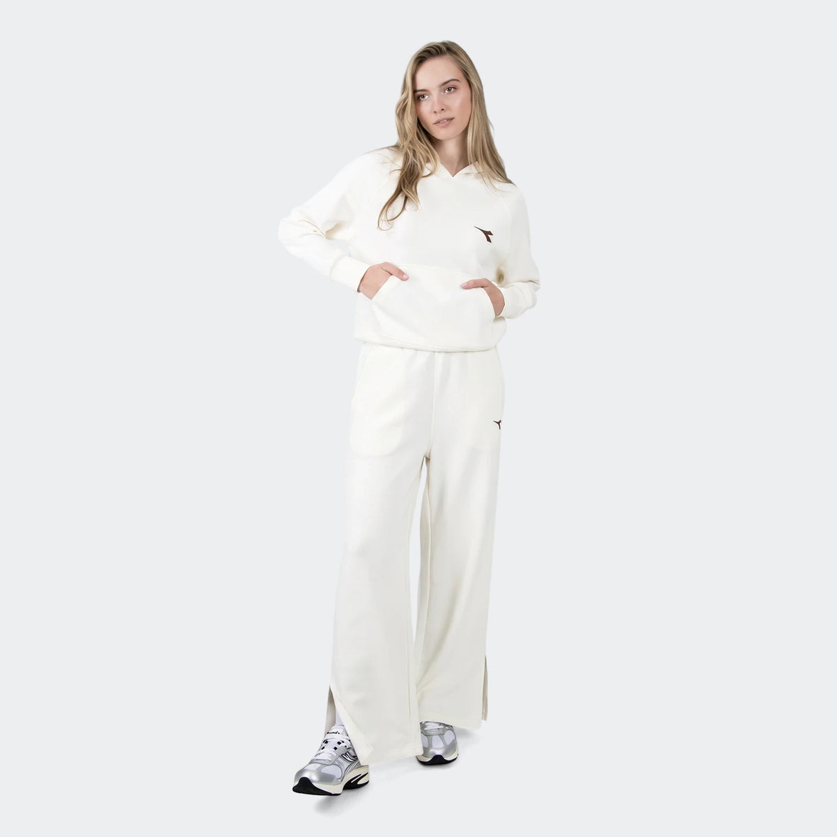 Woman wearing off-white wide-leg Danielle Trackpants and matching hoodie with silver sneakers, full body view.