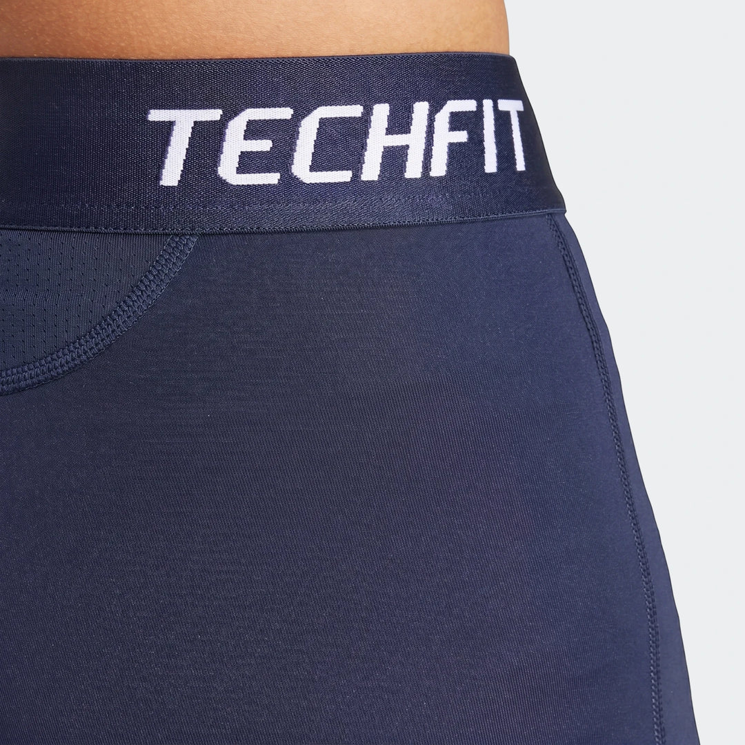 Close-up of dark blue football base layer tights featuring a white 'TECHFIT' logo on the waistband, worn by a person.