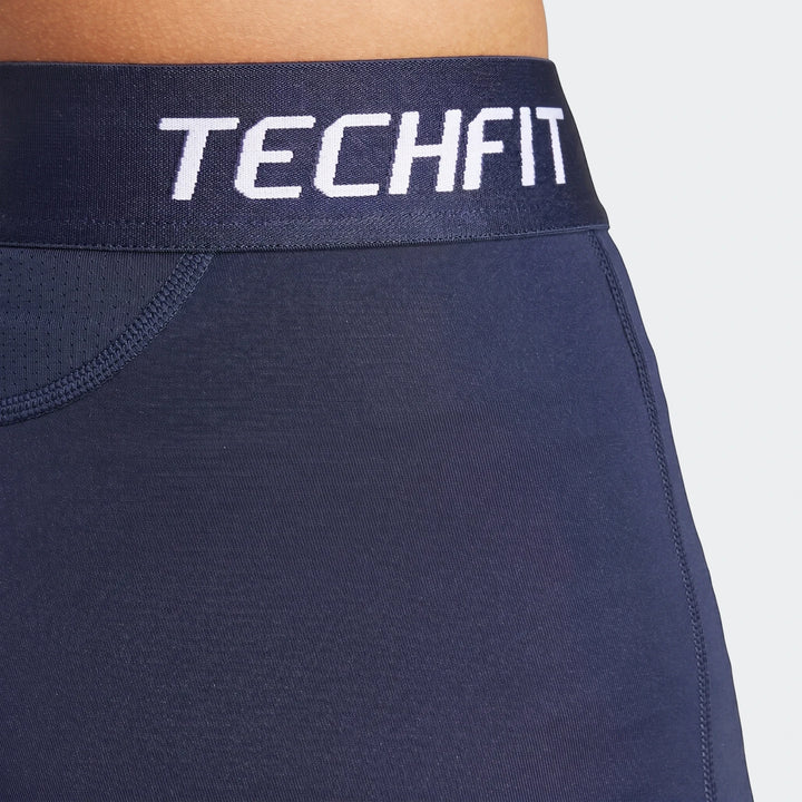 Close-up of dark blue football base layer tights featuring a white 'TECHFIT' logo on the waistband, worn by a person.