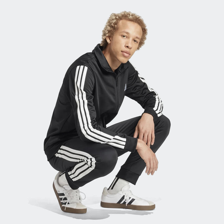 Full-body shot of a man wearing a black Dayready Tracksuit with white stripes and white sneakers, posed in a squat.