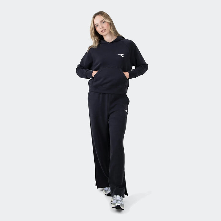 Woman wearing a black Diadora Danielle Trackpant set, featuring a hoodie and wide-leg pants, captured in a full-body studio