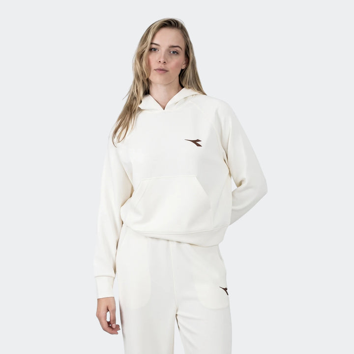 Female model wearing a cream Diadora Michelle Hoodie and matching sweatpants, posing against a clean white studio background.