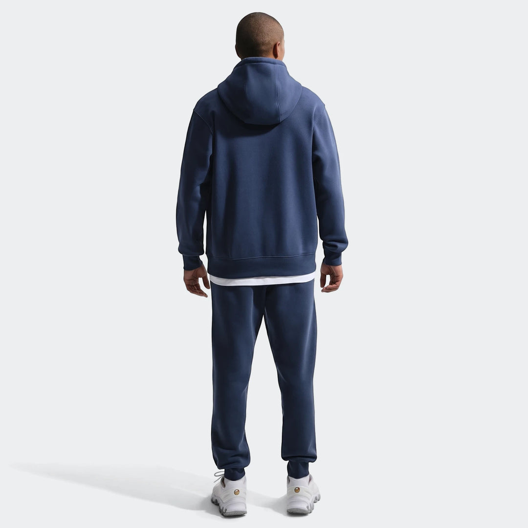 Full body back view of a man wearing an England Club Blue Men's Nike Soccer Pullover Hoodie with matching sweatpants.