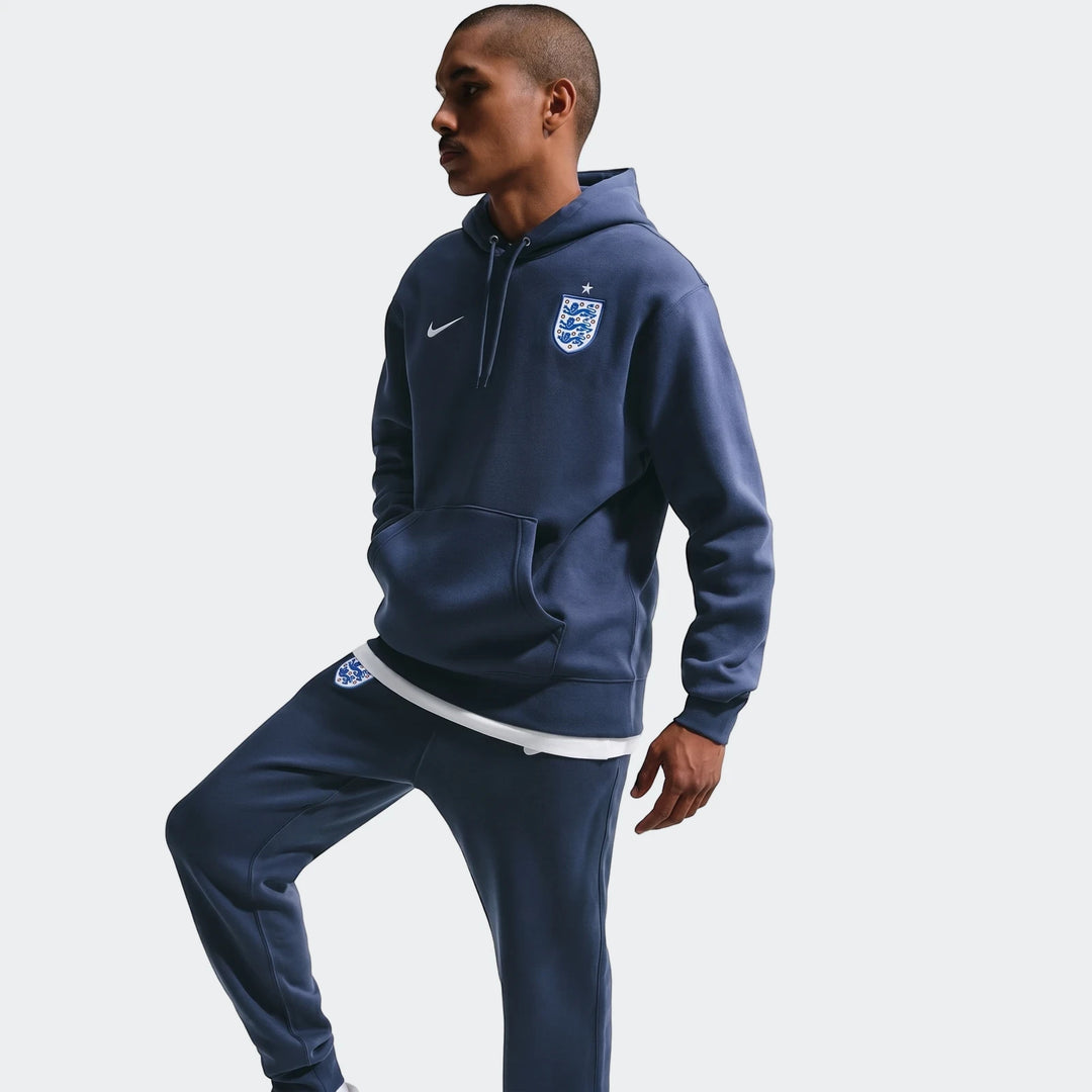 Male model wearing a navy blue Nike England Club men's soccer pullover hoodie and matching sweatpants.