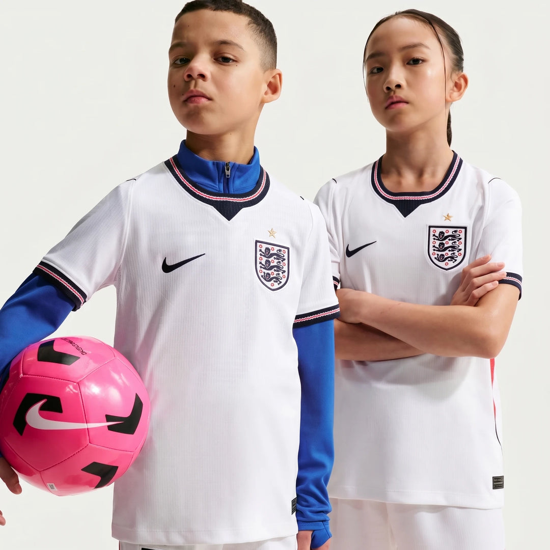 Two kids wearing white England National Team 2026 Stadium Home Nike Dri-Fit soccer jerseys, one boy holding a pink soccer