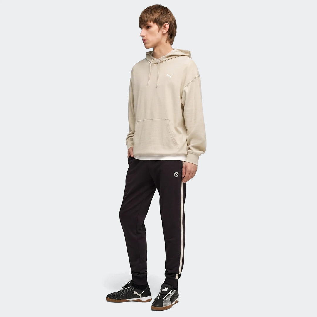 Male model wears Ess Elevated Black Sweatpants, a beige hoodie, and black shoes in a full body side view.