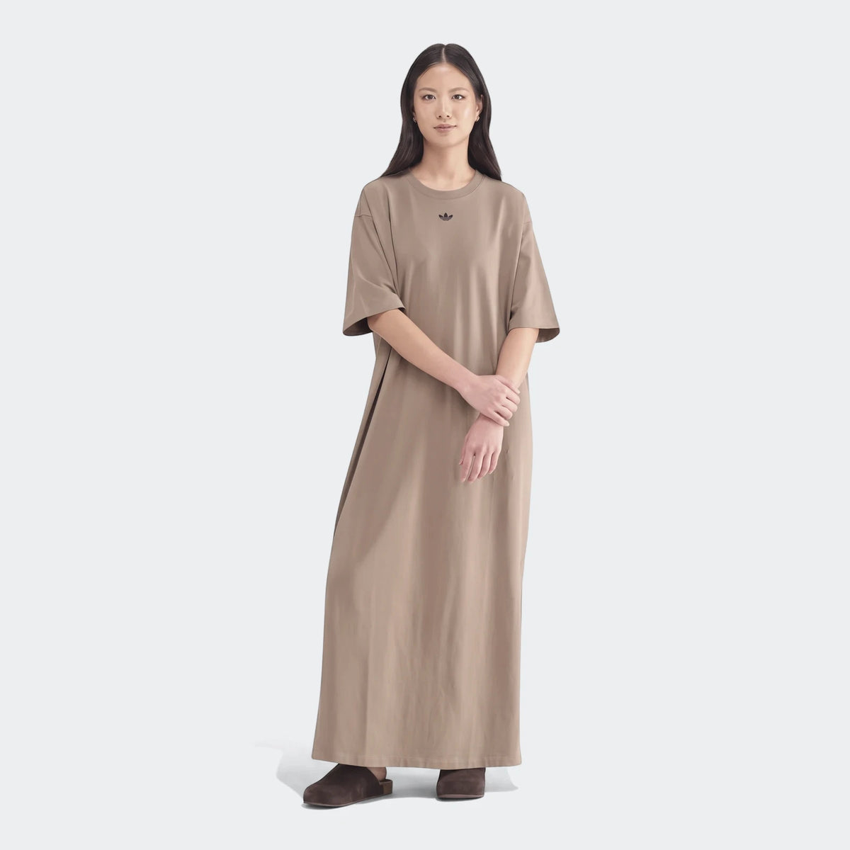 A woman models an Essential Beige Dress, a full-length, short-sleeve t-shirt dress with an Adidas Trefoil logo on the chest.