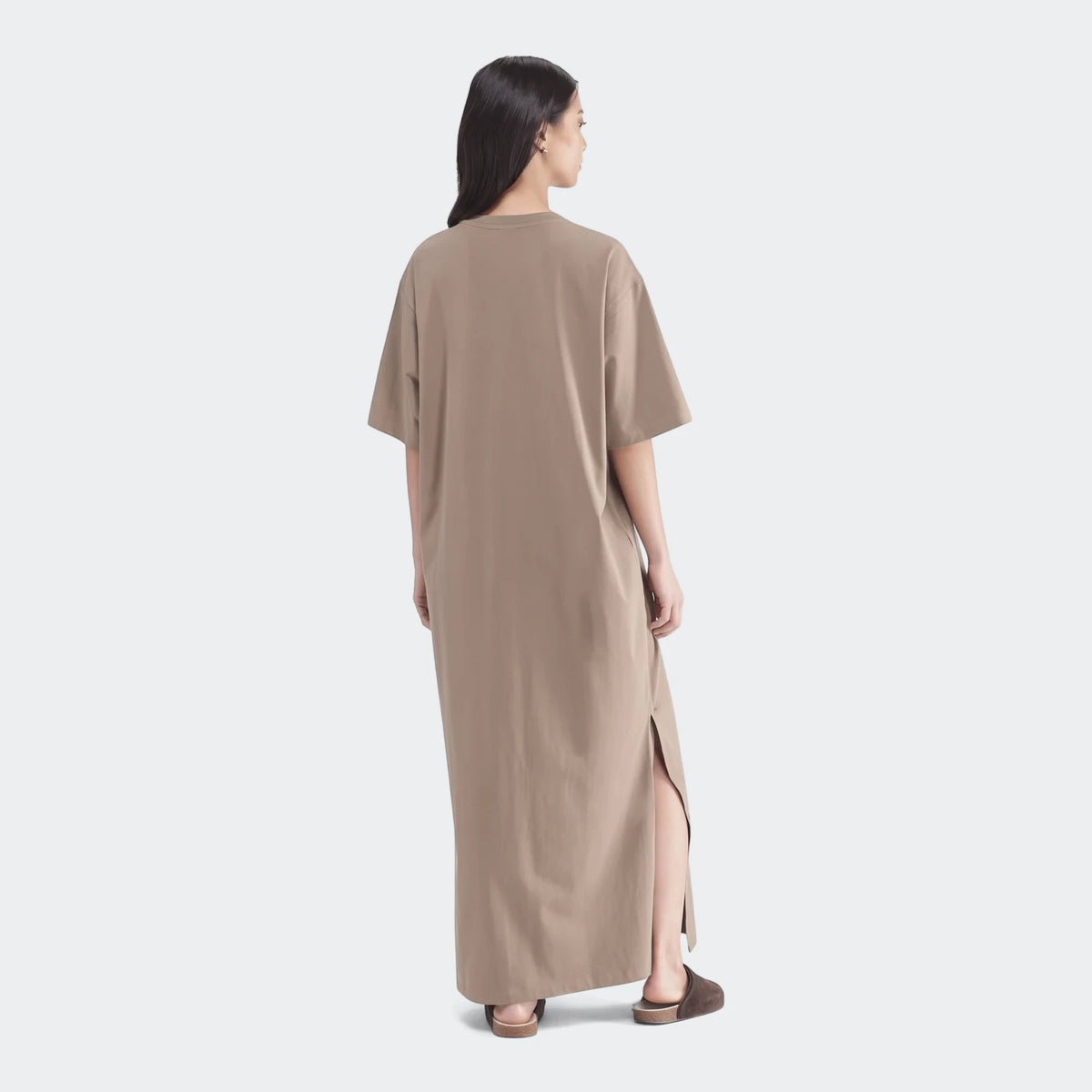Woman wearing a long, short-sleeved essential beige dress, seen from the back, with a side slit for casual wear.