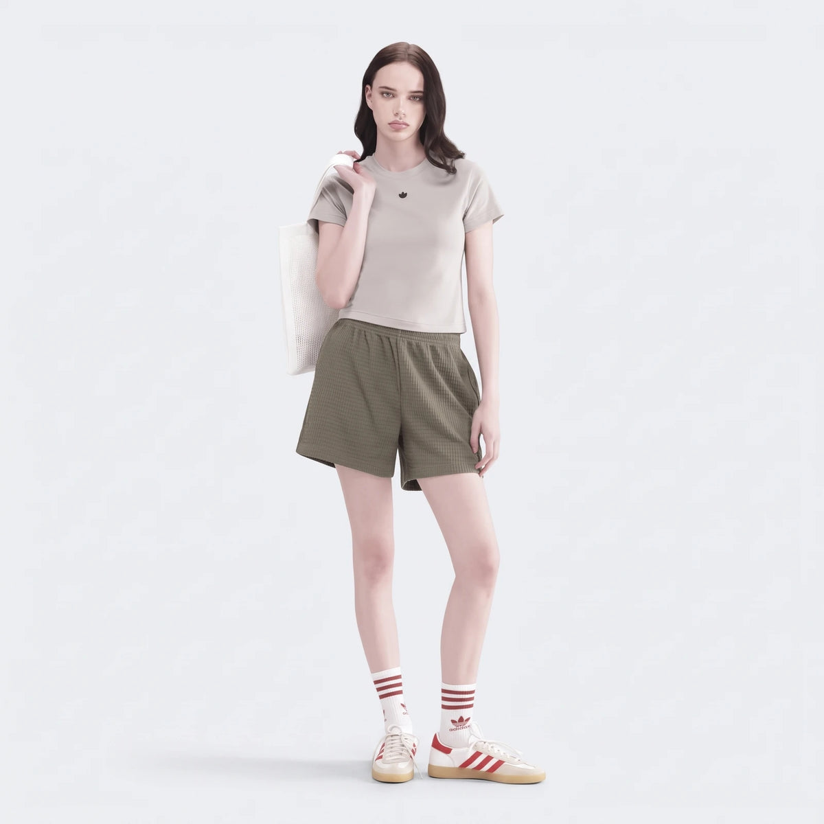 Female model wearing olive green waffle knit essential shorts, a light grey tee, and white red striped sneakers, carrying a