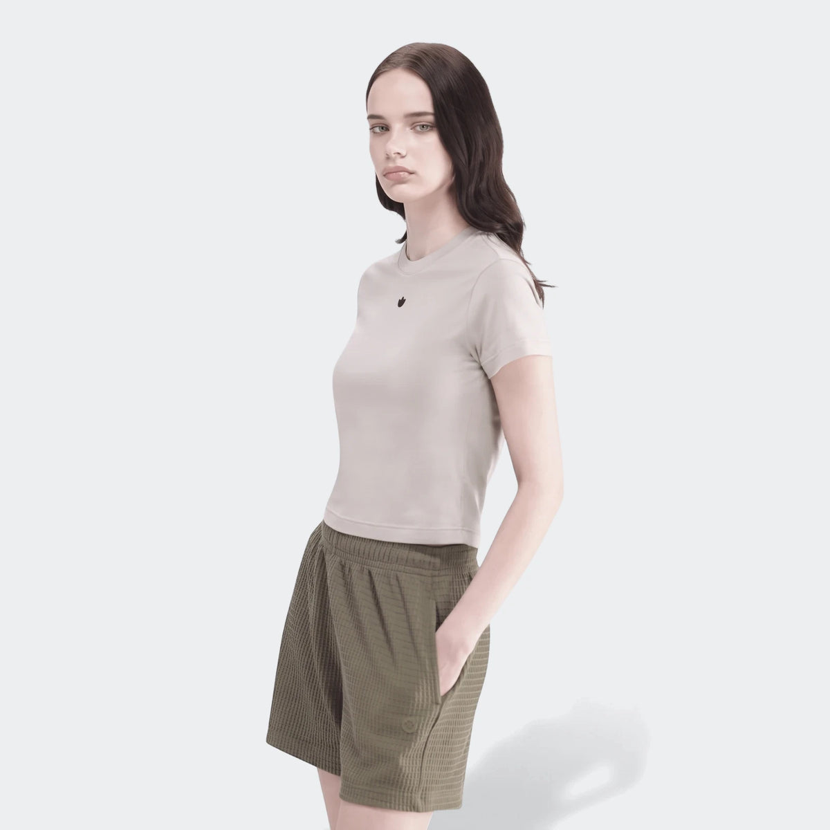 Woman wearing light beige crop top and olive green waffle texture Essential Shorts, posed with hand in pocket.