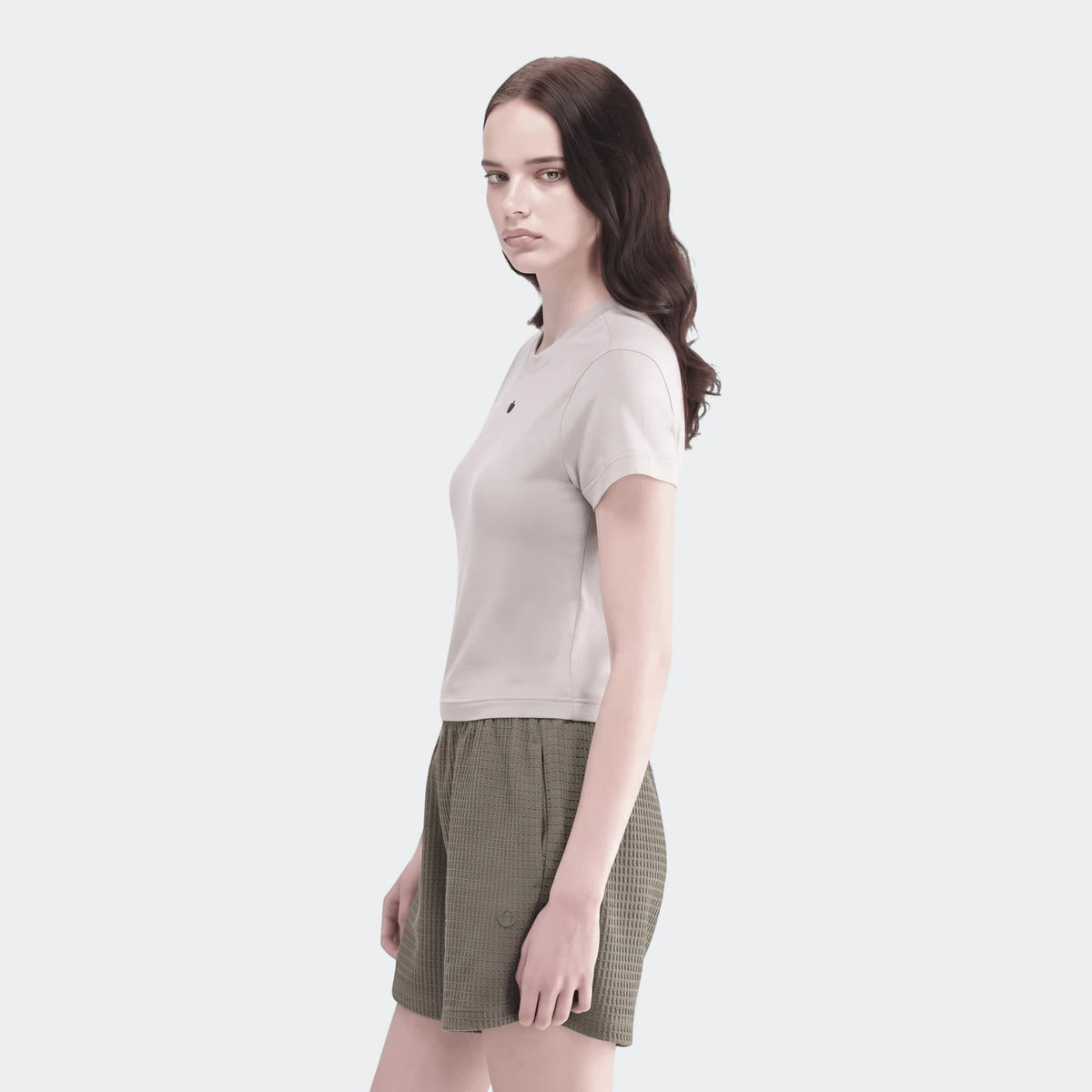 Young woman wearing a light grey t-shirt and olive green waffle knit Essential Shorts, posed in profile looking forward.