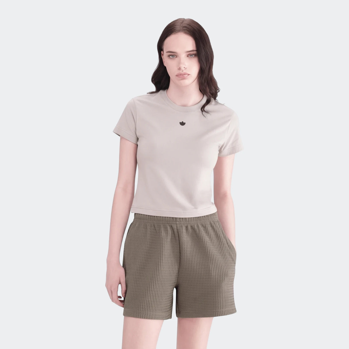 A female model wears olive green waffle knit Essential Shorts and a light grey t-shirt, standing front-facing.