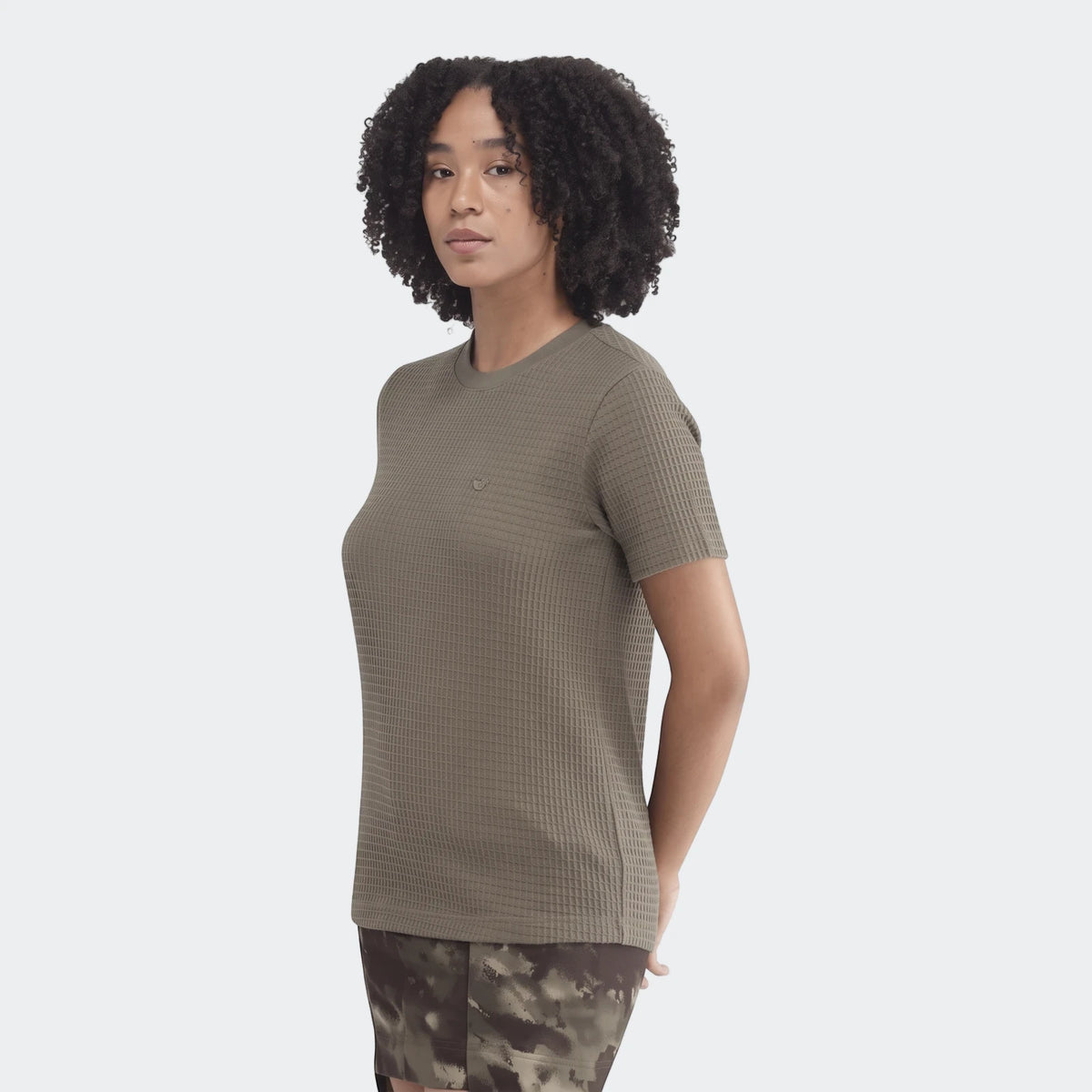 Woman wearing a dark olive green waffle-knit short-sleeve essential t-shirt, posed casually on a white background.