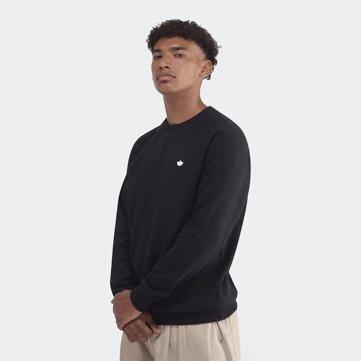 Male model wearing a black Essentials Crew Sweatshirt, facing forward with hands clasped in a studio setting.
