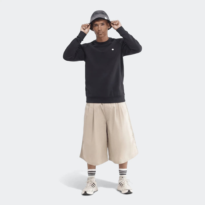 Young man wears a black Essentials Crew Sweatshirt, beige wide-leg shorts, a striped bucket hat, and white sneakers,