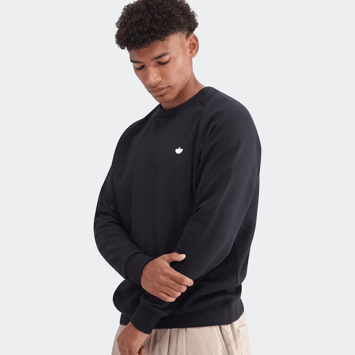 Male model wearing a navy blue Essentials Crew Sweatshirt, front view. The model is looking down with his arms crossed.