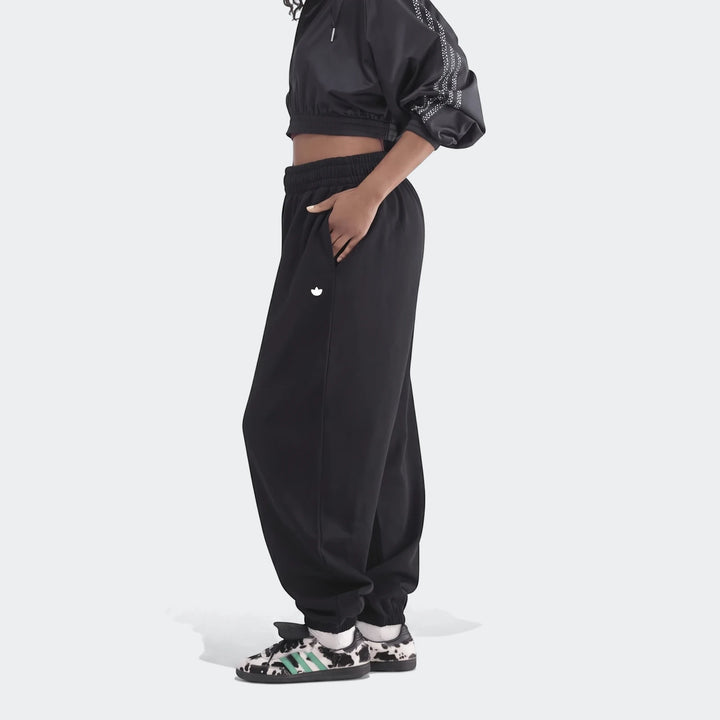 A model wears black Essentials French Terry Jogger Pants and a cropped jacket, paired with unique cow-print sneakers, shown
