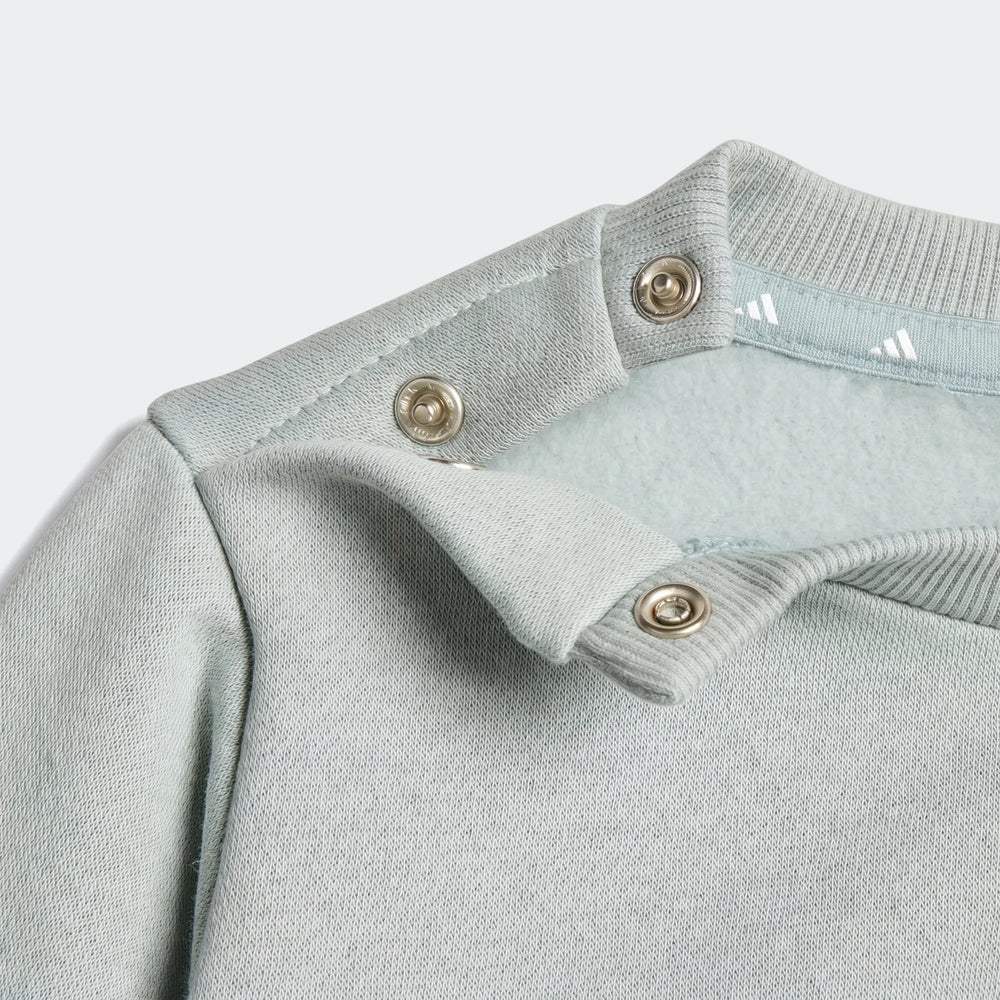 Close-up of a light blue Essentials Joggers Kids long-sleeve top showing the shoulder with snap buttons and ribbed collar