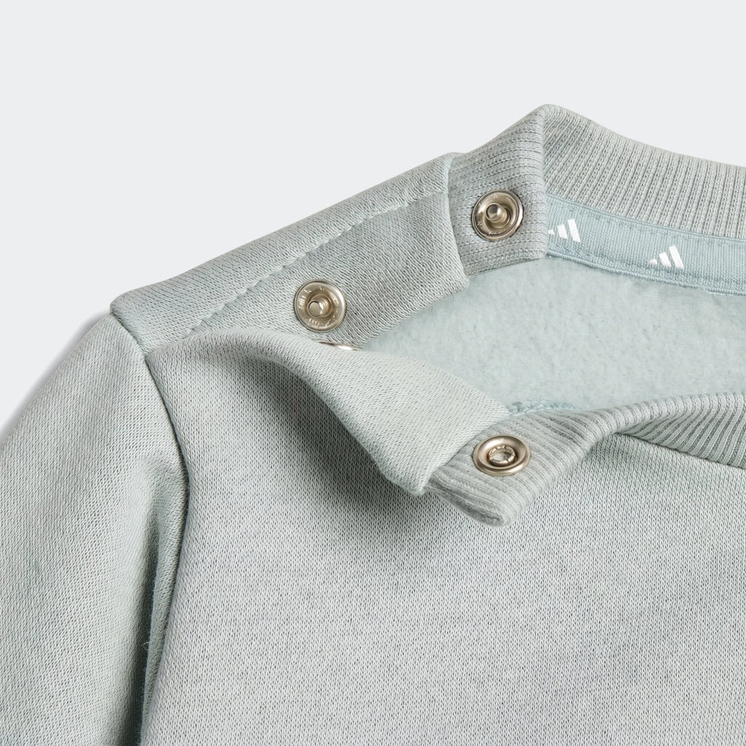 Close-up of a light blue Essentials Joggers Kids long-sleeve top showing the shoulder with snap buttons and ribbed collar