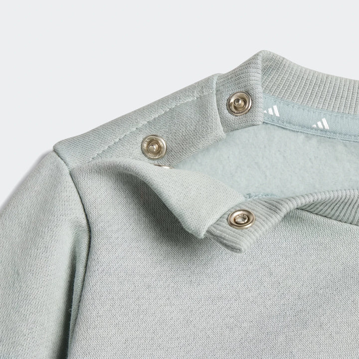 Close-up of a light blue Essentials Joggers Kids long-sleeve top showing the shoulder with snap buttons and ribbed collar