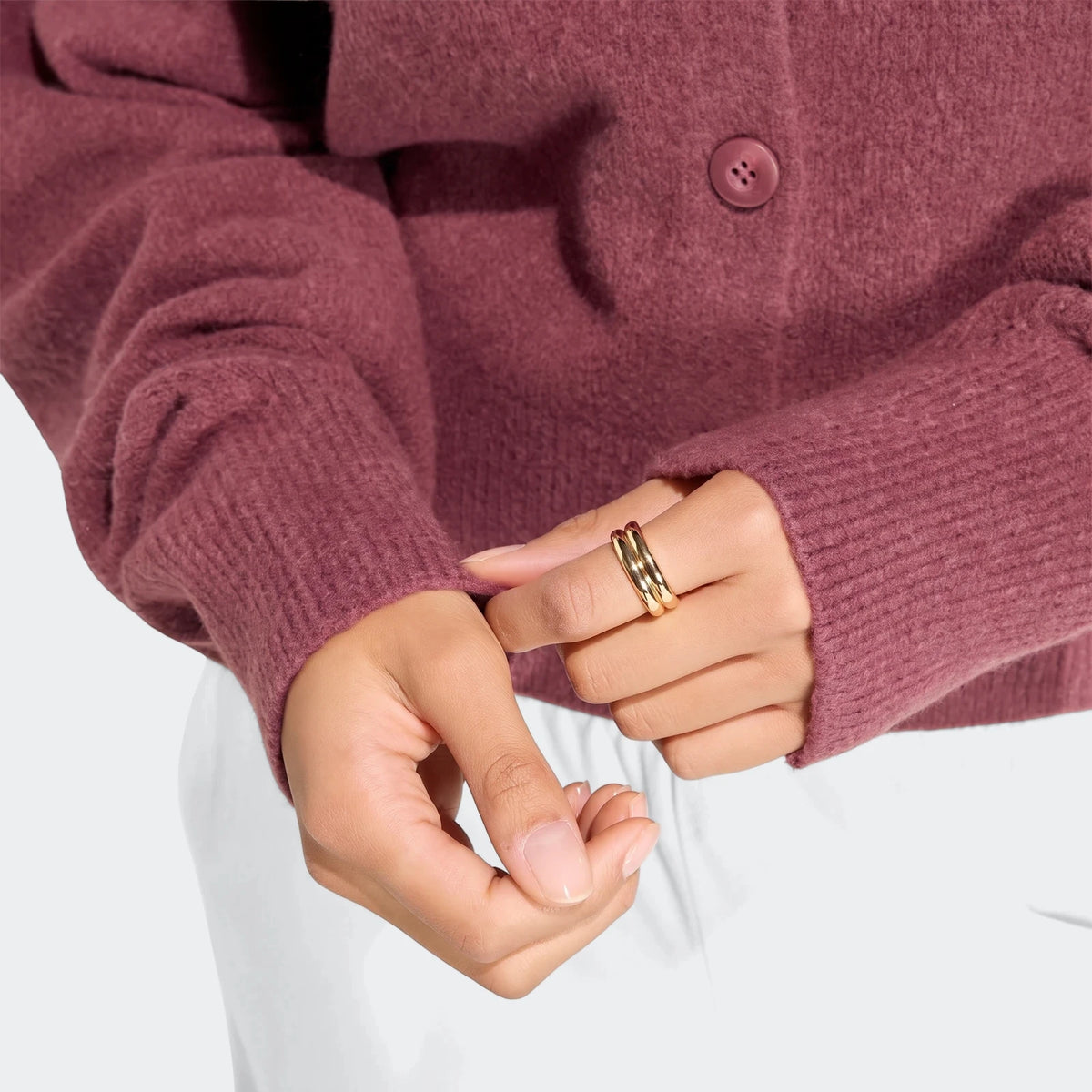 Close-up of a person wearing a magenta knit Essentials Cardigan, with hands adjusting the sleeve cuff, showcasing a gold