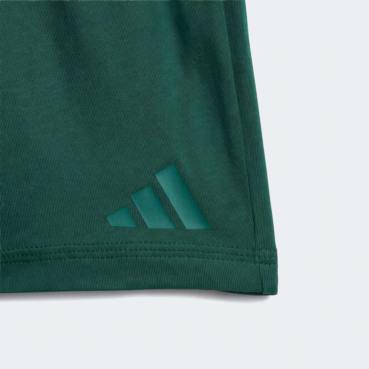 Close-up of a dark green Essentials Tee Set Kids garment, showcasing the Adidas logo and fabric texture.