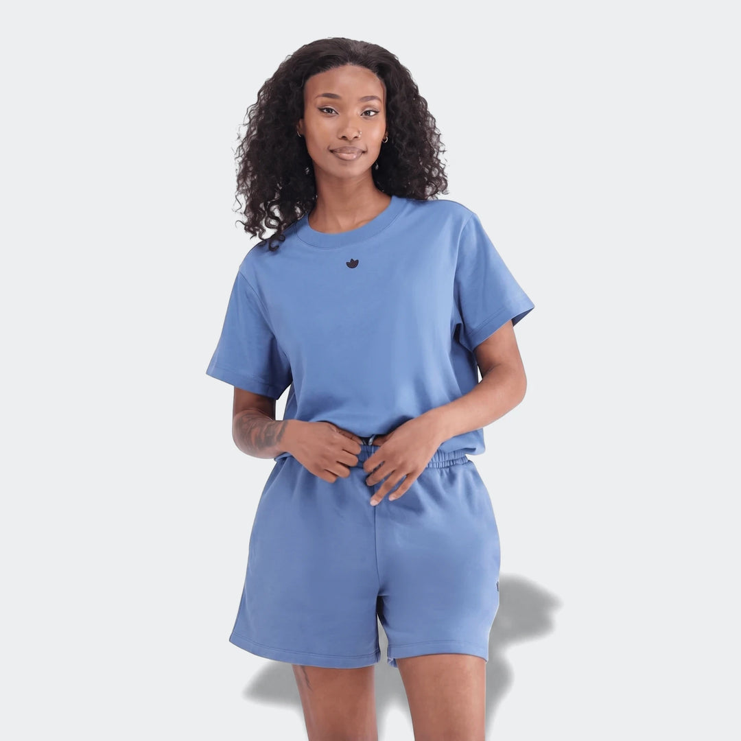 Woman models a blue Essentials Trefoil T-Shirt and matching shorts in a full-body shot, showcasing the casual athletic wear.