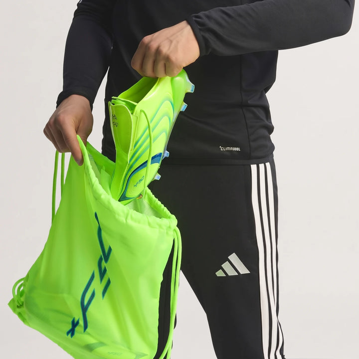 Person's hands putting a neon green Adidas F50 Elite Fg Tunit football boot into a matching drawstring bag, wearing black