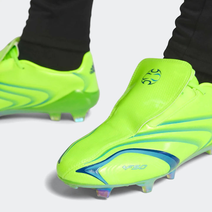 Close-up of neon green Adidas F50 Elite Fg Tunit football boots with blue accents, worn on feet.