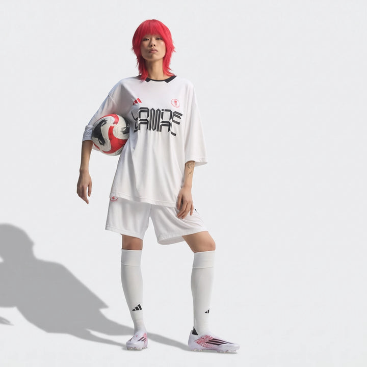 Female model in white F50 Elite LL FG Lamine Yamal football boots, white jersey, and shorts, holding a soccer ball.