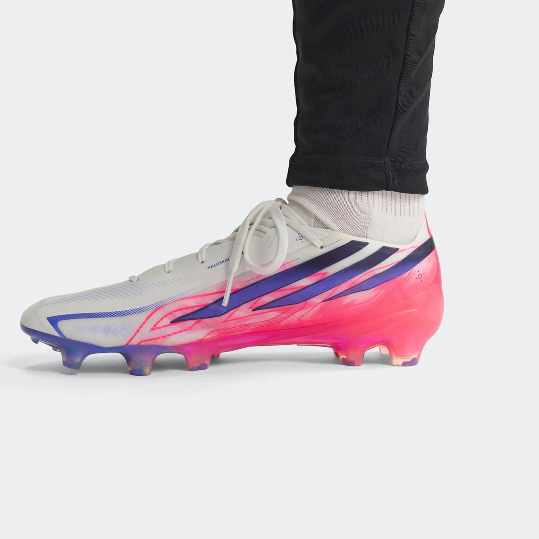 Close-up of a white, pink, and purple F50 Hyperfast Elite Firm Ground Football Boot with laces, worn on a person's foot.
