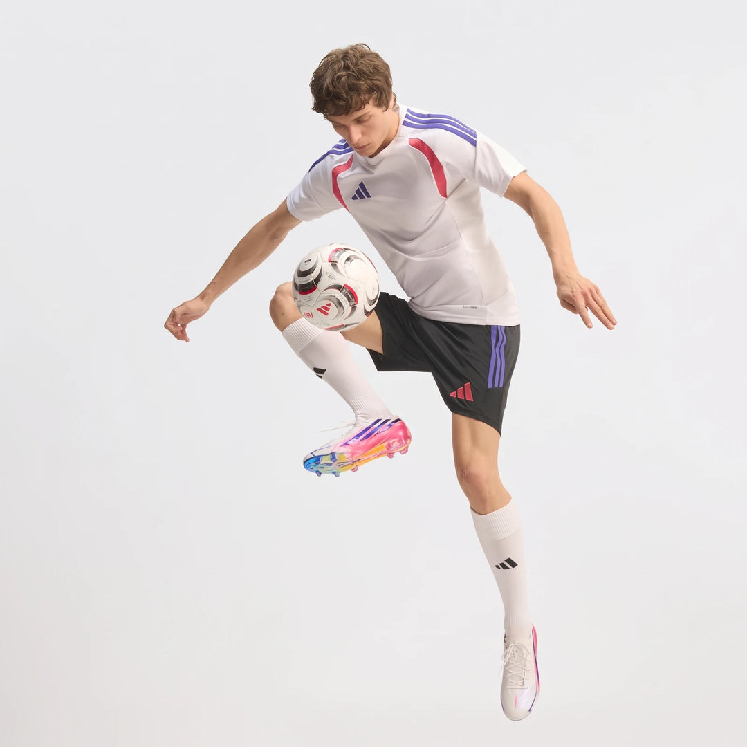 Male soccer player in F50 Hyperfast Elite Firm Ground Football Boots, white jersey, and black shorts, juggling a soccer ball