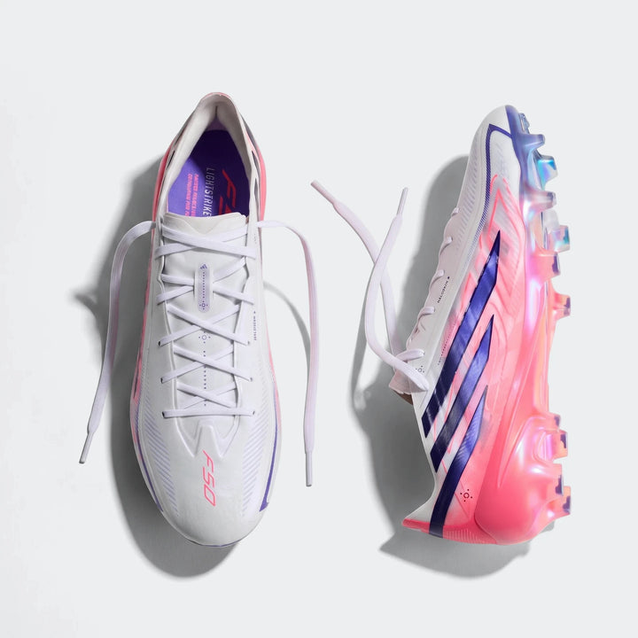 Overhead view of white, pink, and purple F50 Hyperfast Elite Firm Ground Football Boots with iridescent soles and untied