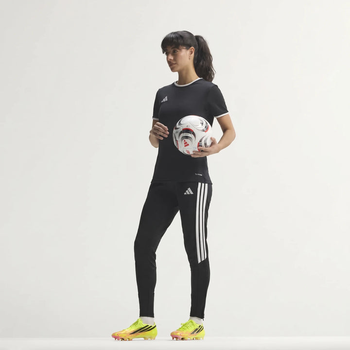 Woman in black Adidas training kit, holding a soccer ball and wearing yellow F50 Hyperfast Elite Firm Ground Football Boots.