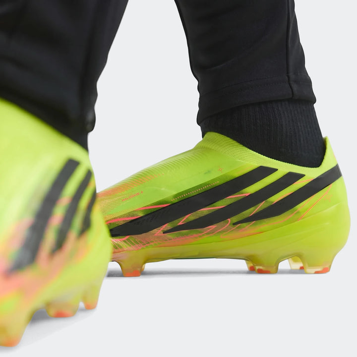 Close-up of F50 Hyperfast Elite Laceless Firm Ground Boots in neon yellow-green with black stripes, worn by a person on a