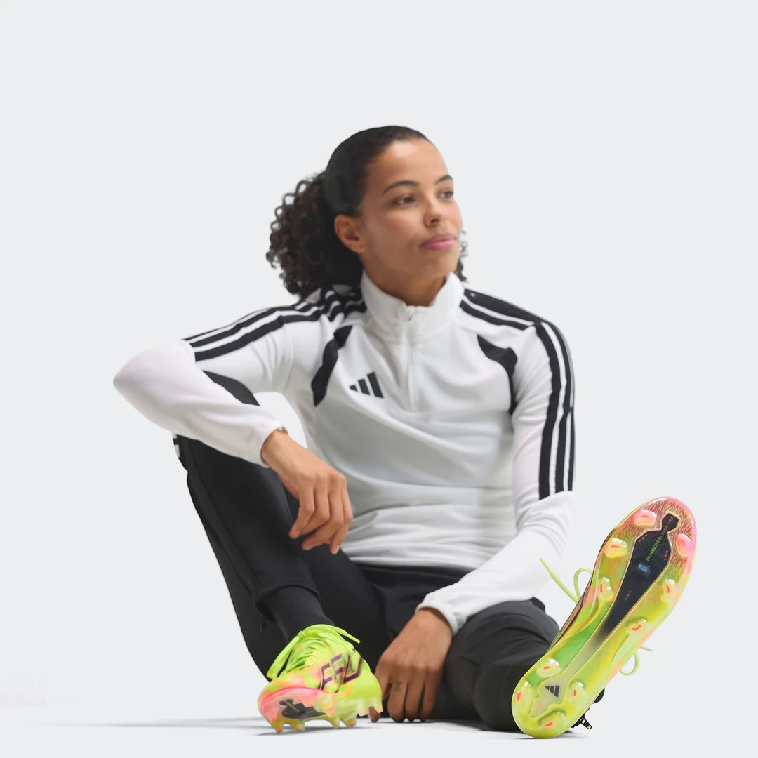 Female model wears a white Adidas top, black pants, and neon yellow and pink F50 Hyperfast Evo Firm Ground Football Boots in