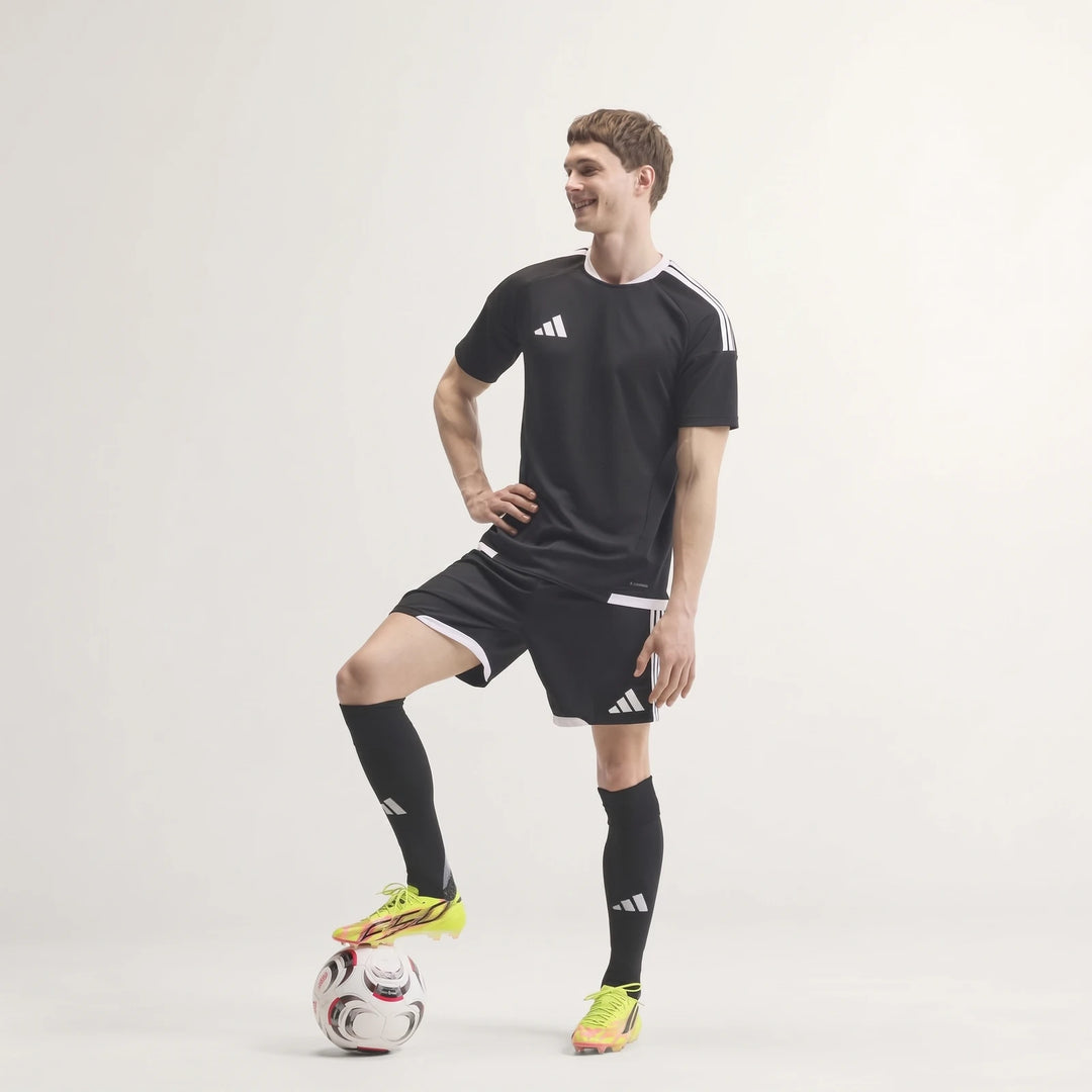 Male model wearing F50 Hyperfast Evo Firm Ground Football Boots in neon yellow/pink, black soccer kit, standing with foot on