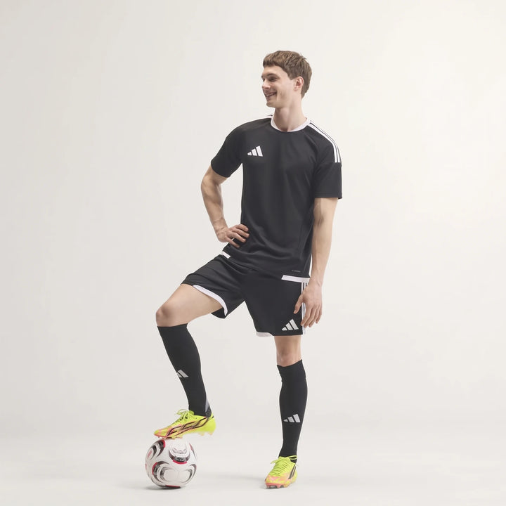 Male model wearing F50 Hyperfast Evo Firm Ground Football Boots in neon yellow/pink, black soccer kit, standing with foot on