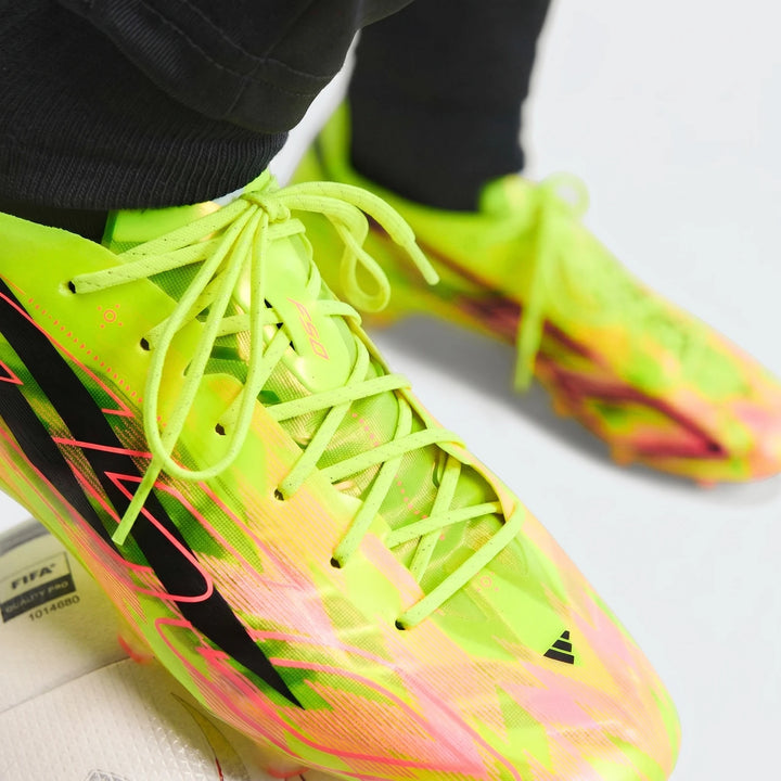 Close-up of F50 Hyperfast Evo Firm Ground Football Boots in vibrant neon yellow and pink, worn on feet with black socks.