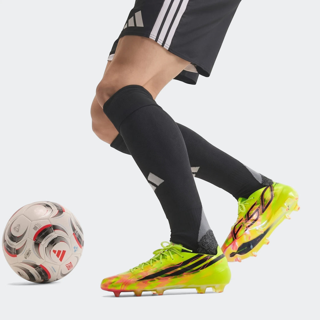 Close-up of a soccer player wearing neon yellow F50 Hyperfast Evo Firm Ground Football Boots, black shorts, and black socks,